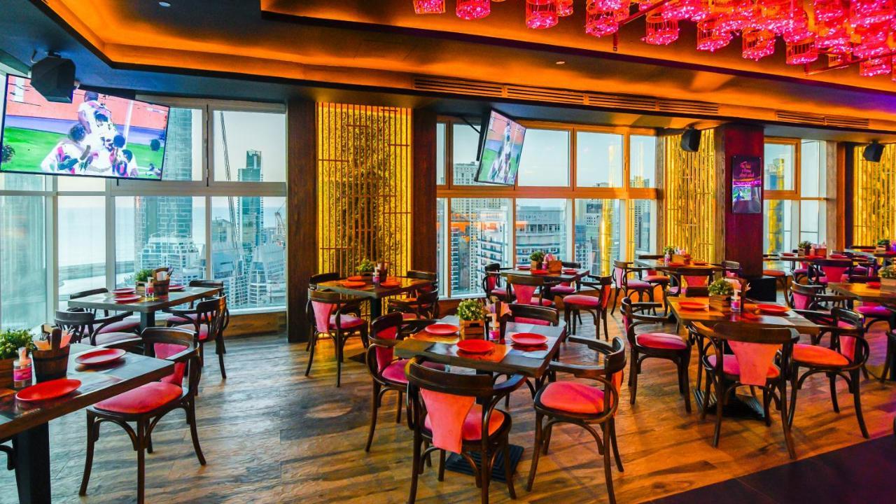 Stella Di Mare Dubai Marina Hotel Esterno foto The photo shows a stylish restaurant interior with multiple dining tables arranged neatly. The tables are round with dark wooden surfaces and feature bright red chairs with cushioned seats. The decor includes warm lighting, with accents of pink and g