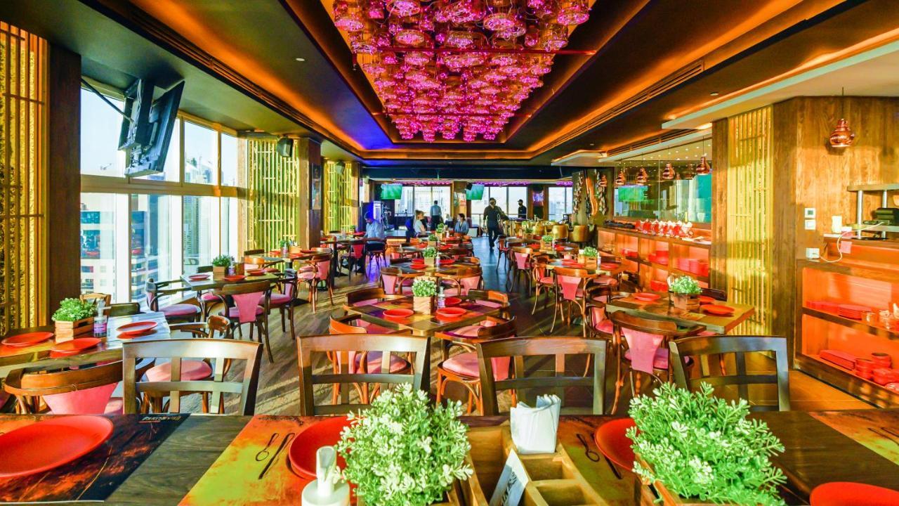 Stella Di Mare Dubai Marina Hotel Esterno foto The photo depicts a vibrant restaurant interior featuring a modern and stylish design. The space has a warm ambiance with wooden furniture and colorful table settings, including red plates and greenery centerpieces. The ceiling is adorned with a stri