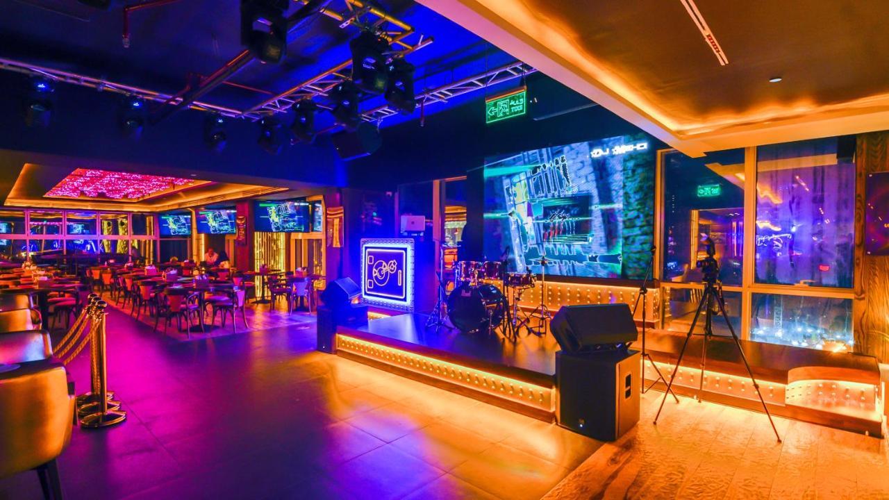Stella Di Mare Dubai Marina Hotel Esterno foto The photo showcases a vibrant nightlife setting, likely a bar or club. The interior is illuminated with colorful lights, primarily purples and blues, creating a lively atmosphere. There are tables and chairs arranged for patrons, and a stage area equ