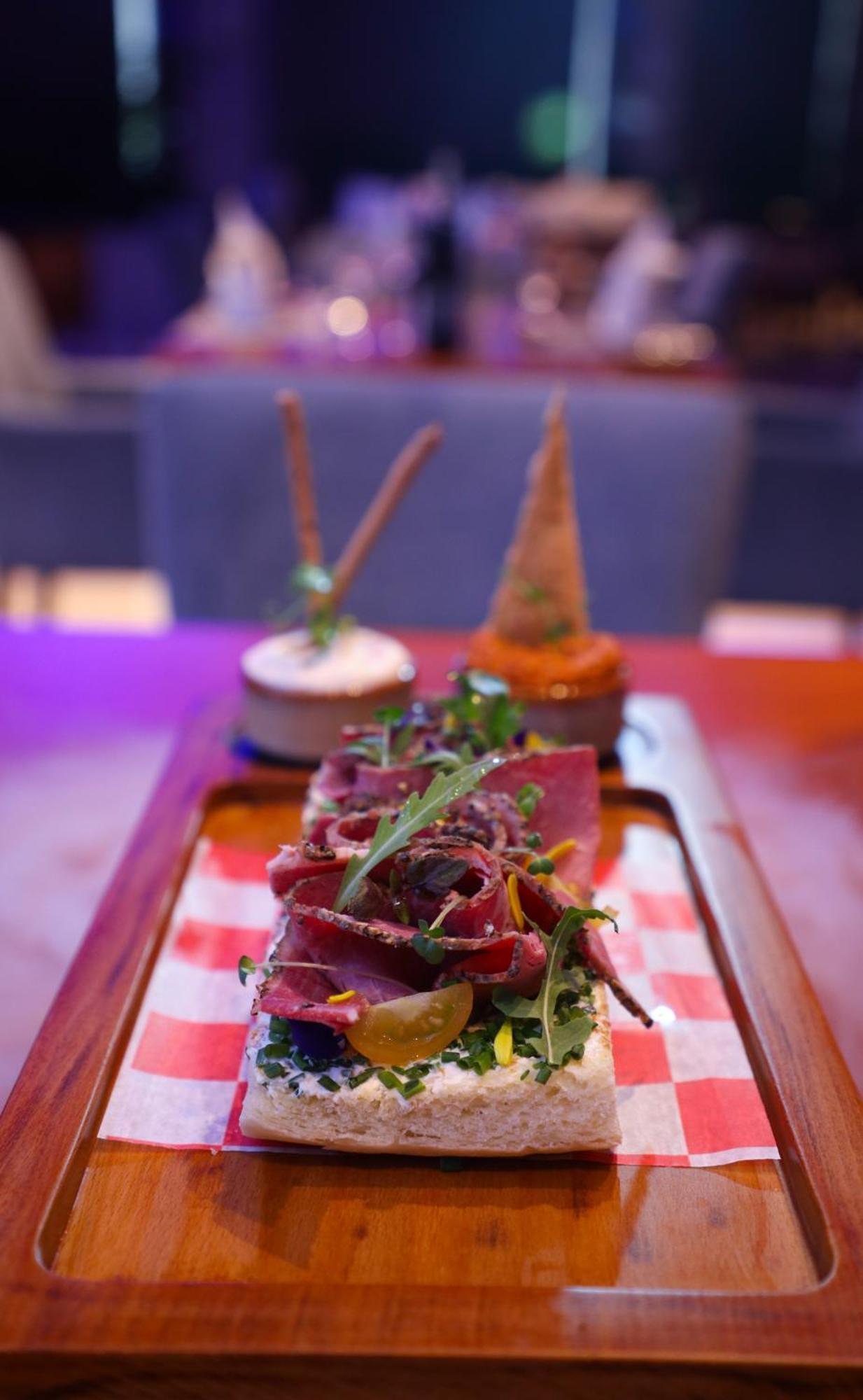 Stella Di Mare Dubai Marina Hotel Esterno foto The photo showcases a beautifully presented dish. In the foreground, there is a plate featuring thinly sliced meat topped with fresh greens and garnishes. It appears to be served on a wooden platter with a red and white checkered paper underneath. In