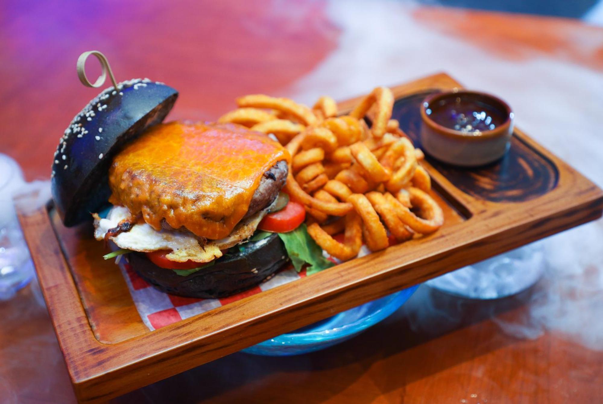 Stella Di Mare Dubai Marina Hotel Esterno foto The photo shows a delicious meal presented on a wooden tray. It features a burger with a black sesame seed bun, which is topped with a melted cheese slice. Inside the burger are layers of meat, lettuce, and tomato. Accompanying the burger are curly f