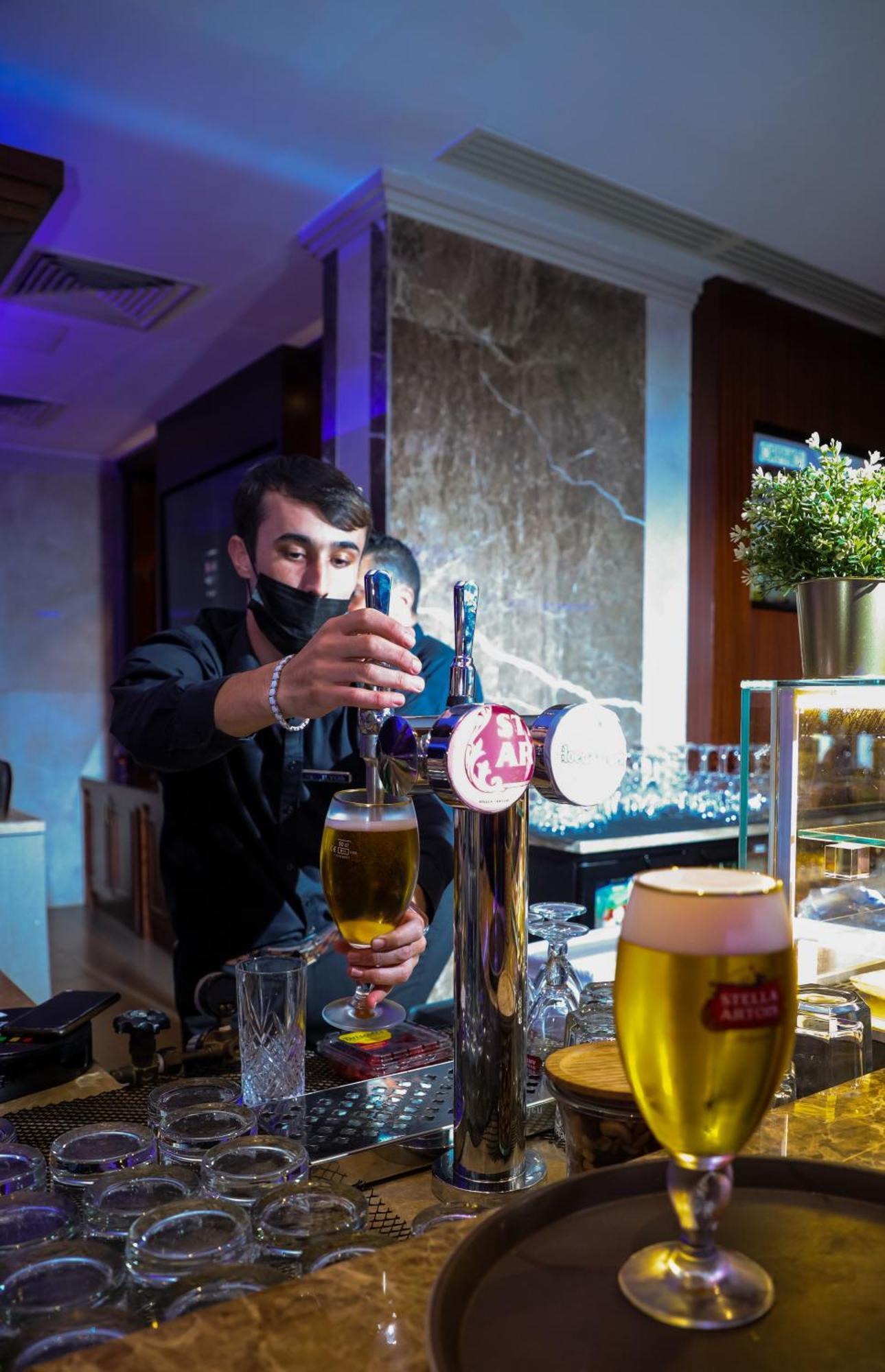 Stella Di Mare Dubai Marina Hotel Esterno foto The photo shows a bartender pouring a beer from a tap. The bartender is wearing a black shirt and a mask. In the background, there are several glasses and a bar setup with a modern design. The scene appears to be in a well-lit bar or lounge environme