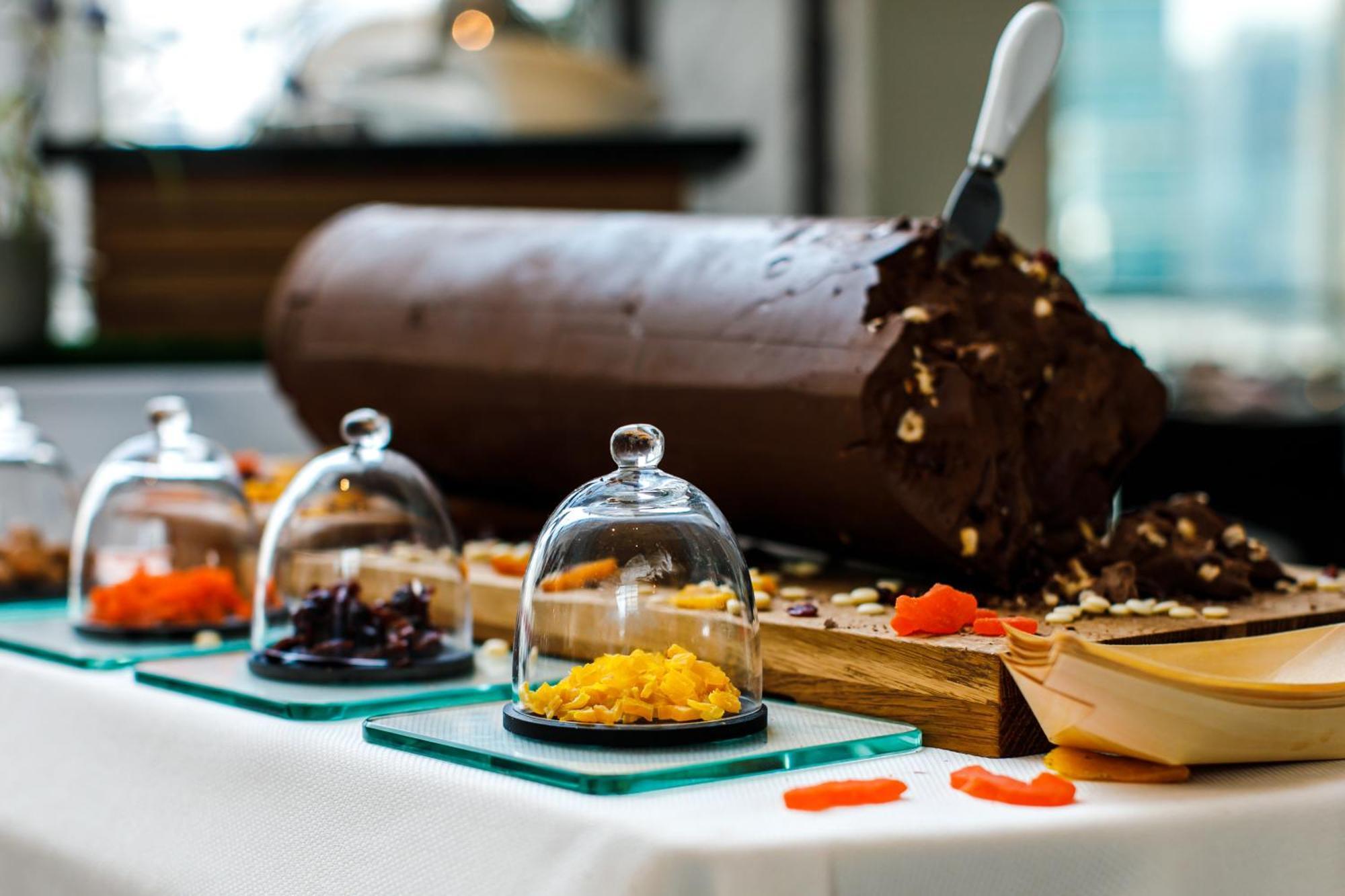 Stella Di Mare Dubai Marina Hotel Esterno foto The photo showcases a dessert display featuring a large yule log cake or chocolate roll, which is rich and decorated with various toppings. In front of the cake, there are three small glass cloches, each containing different colorful toppings or garn