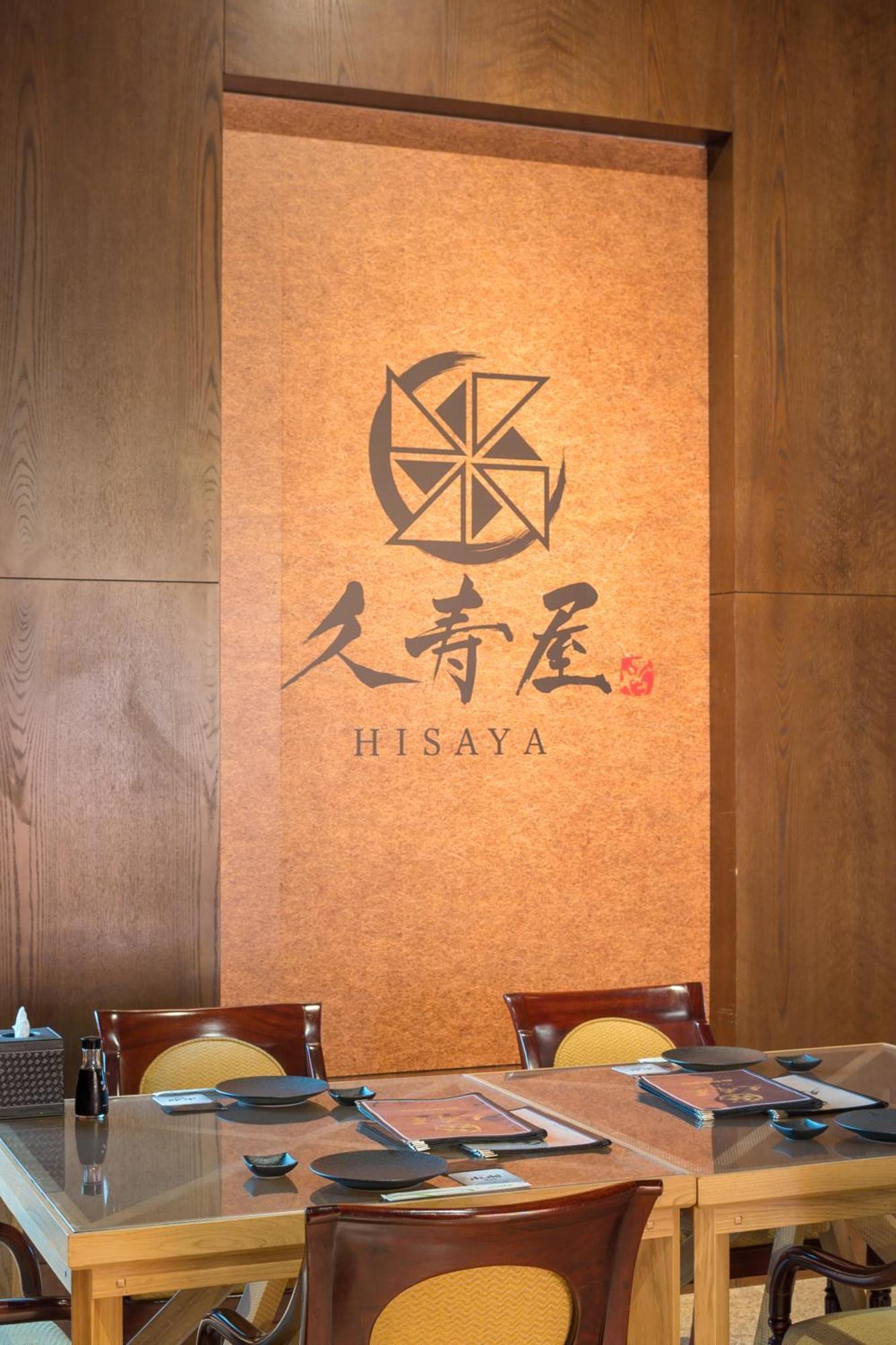 Stella Di Mare Dubai Marina Hotel Esterno foto The photo shows a wall featuring the logo of a place called "Hisaya." The logo includes a stylized emblem that resembles a circular design, possibly a compass or a flower shape, situated above the name "HISAYA," which is written in a combination of E