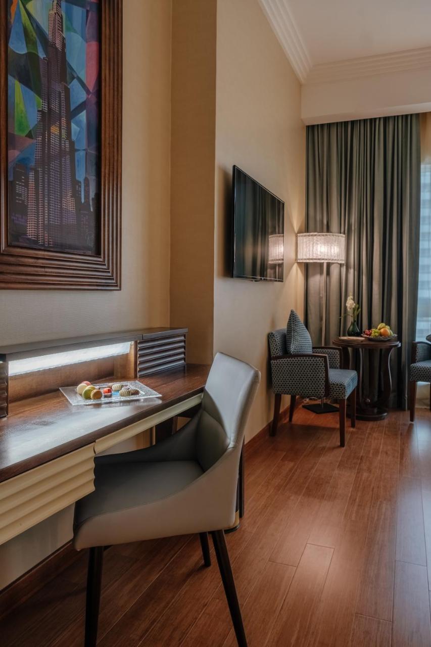 Stella Di Mare Dubai Marina Hotel Esterno foto The photo shows a cozy hotel room or suite. On one side, there is a wooden desk with a small tray of fruit. Nearby, there's a modern chair. In the background, a flat-screen TV is mounted on the wall, and curtains drape beside it. There's also a small