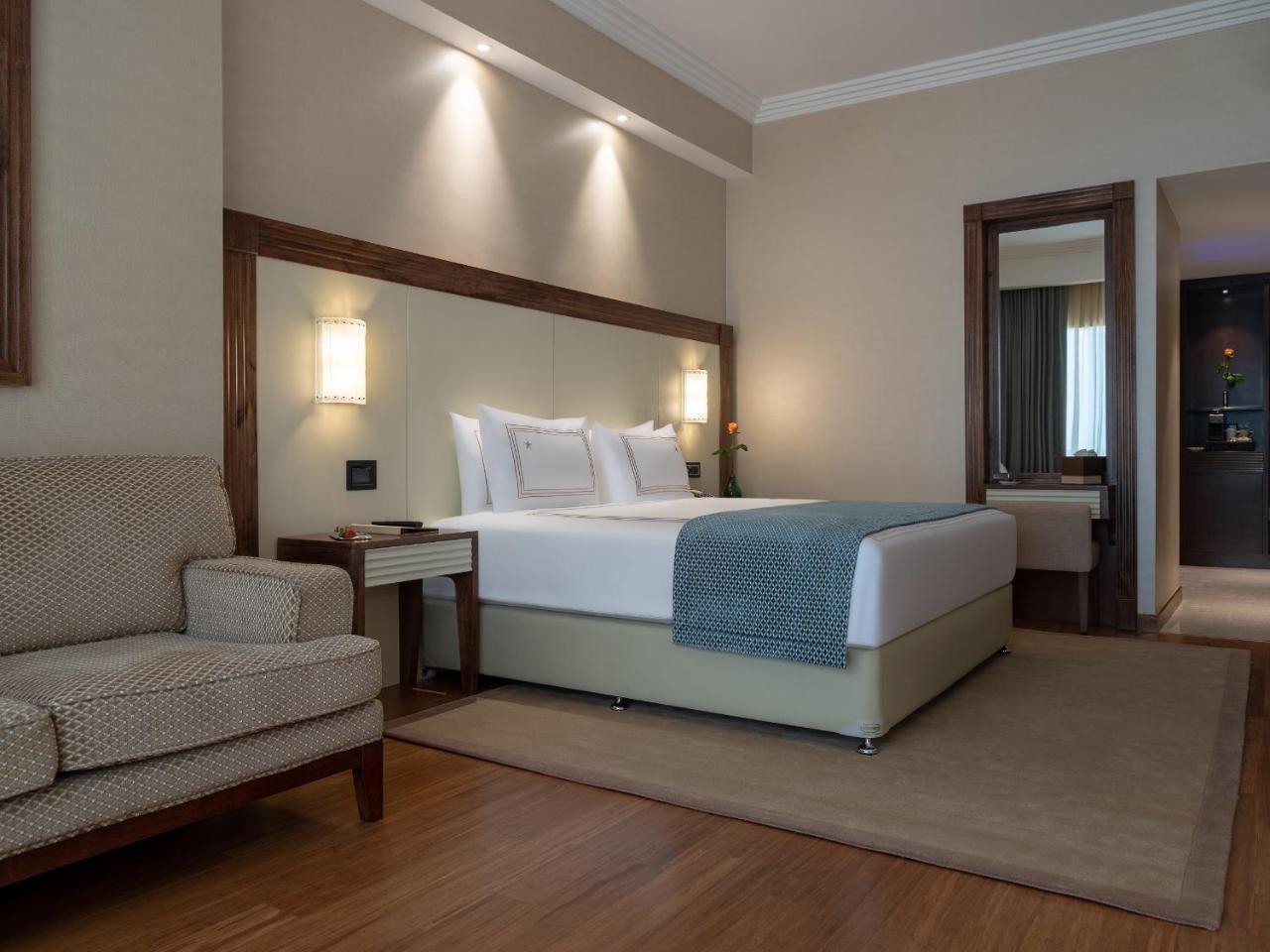 Stella Di Mare Dubai Marina Hotel Esterno foto The photo shows a modern hotel room. It features a large bed with a light-colored headboard and two white pillows. Next to the bed is a small bedside table with a lamp. There is a comfortable armchair in a neutral tone, placed near the bed. The floor