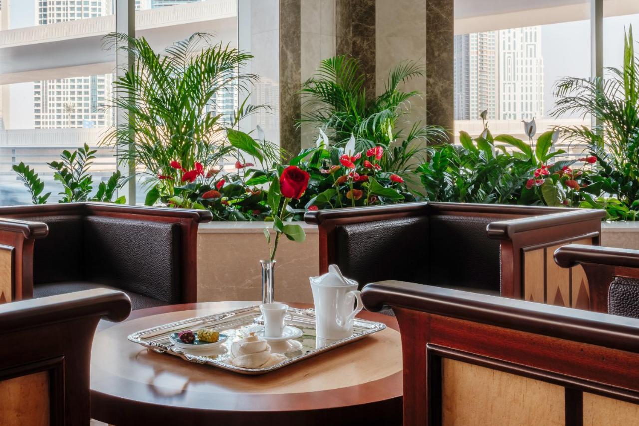 Stella Di Mare Dubai Marina Hotel Esterno foto The photo shows an inviting indoor setting, likely from a restaurant or hotel lobby. In the center, there is a wooden table with a tray that holds a white teapot, a small vase with a single red rose, and some snacks or pastries. Surrounding the table