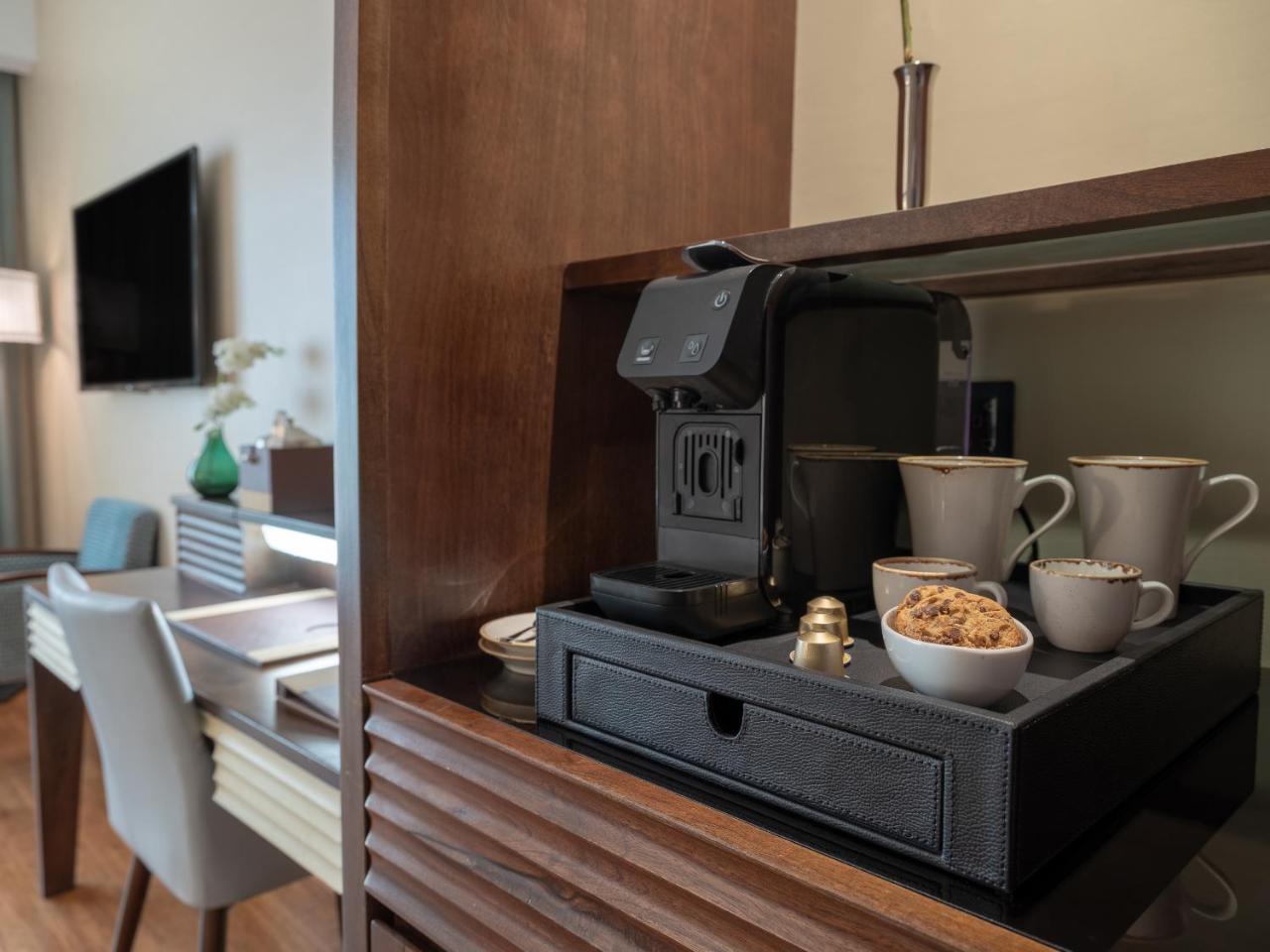 Stella Di Mare Dubai Marina Hotel Esterno foto The photo showcases a cozy corner of a room featuring a coffee machine on a tray. There are several cups arranged next to the machine, which appears to be a single-serve coffee maker. The tray also holds a small container of cookies or snacks. In the