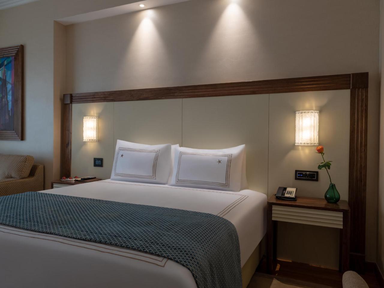 Stella Di Mare Dubai Marina Hotel Esterno foto The photo shows a stylish hotel room with a focus on a large bed adorned with white pillows and a turquoise blanket. The headboard is a light-colored, smooth panel, and on either side of the bed, there are wall-mounted lamps providing soft lighting. 