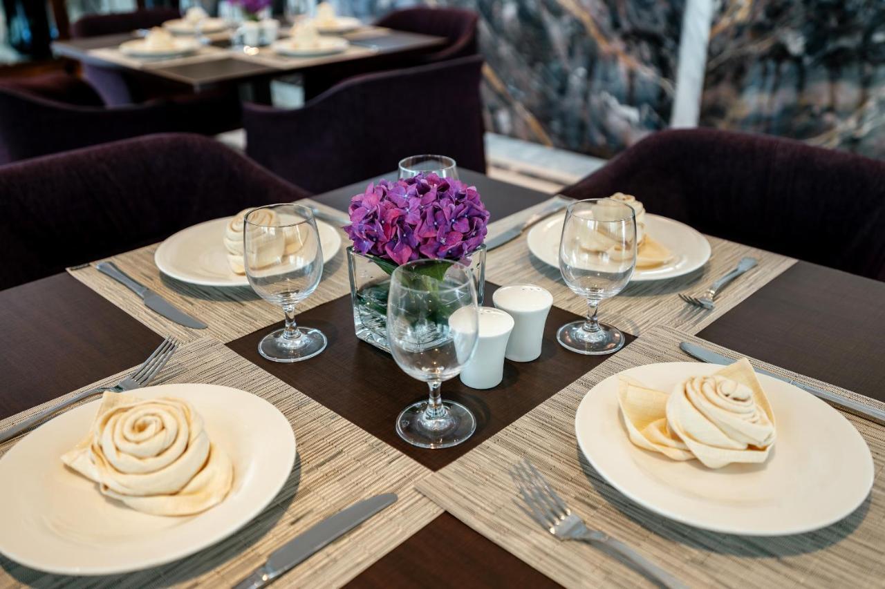 Stella Di Mare Dubai Marina Hotel Esterno foto The photo shows a beautifully set dining table. The table features elegant place settings with white plates arranged in a circular manner. Each plate has a spiral-shaped napkin, resembling a rose. 

There are clear wine glasses beside each plate, and