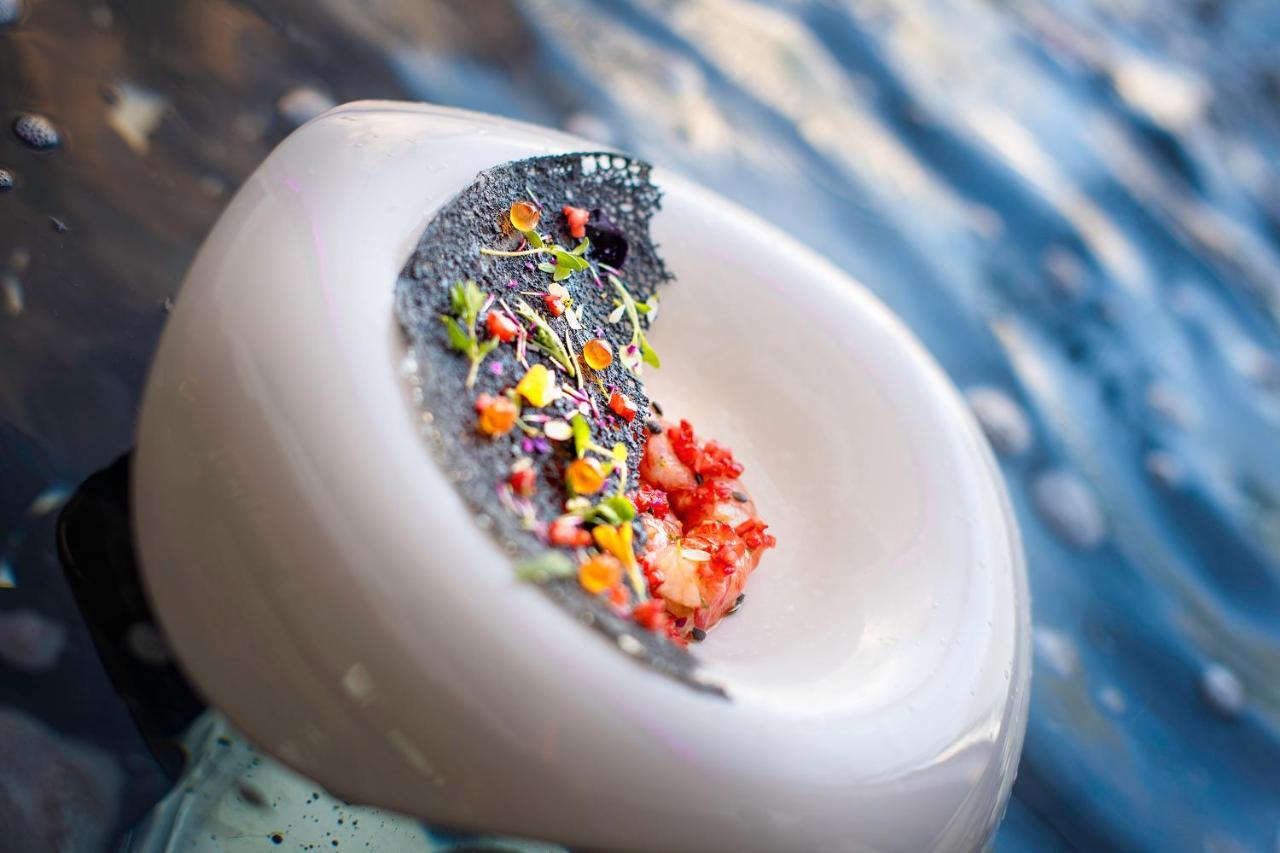 Stella Di Mare Dubai Marina Hotel Esterno foto The photo shows a creatively presented dish that features a circular white plate. On the plate, there is a mound of colorful ingredients, including small bits of meat (likely seafood) and various vibrant garnishes in different colors. The dish appear