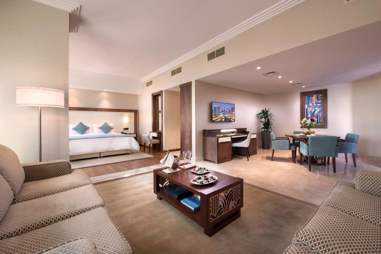 Stella Di Mare Dubai Marina Hotel Esterno foto The photo shows a modern hotel suite featuring a spacious living area and a separate sleeping area. In the living room, there is a comfortable sofa facing a coffee table, which has some decorative items or snacks on it. The suite is decorated with li