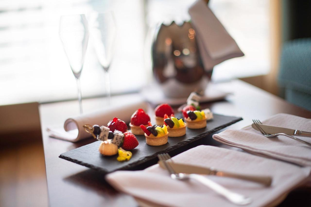 Stella Di Mare Dubai Marina Hotel Esterno foto The photo displays an elegant dessert presentation on a dark slate platter. There are several small pastries topped with vibrant fruits, including strawberries and a yellow cream filling. In the background, two champagne flutes can be seen, along wit